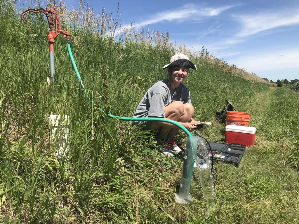 Geology student collects a groundwater sample in a green field